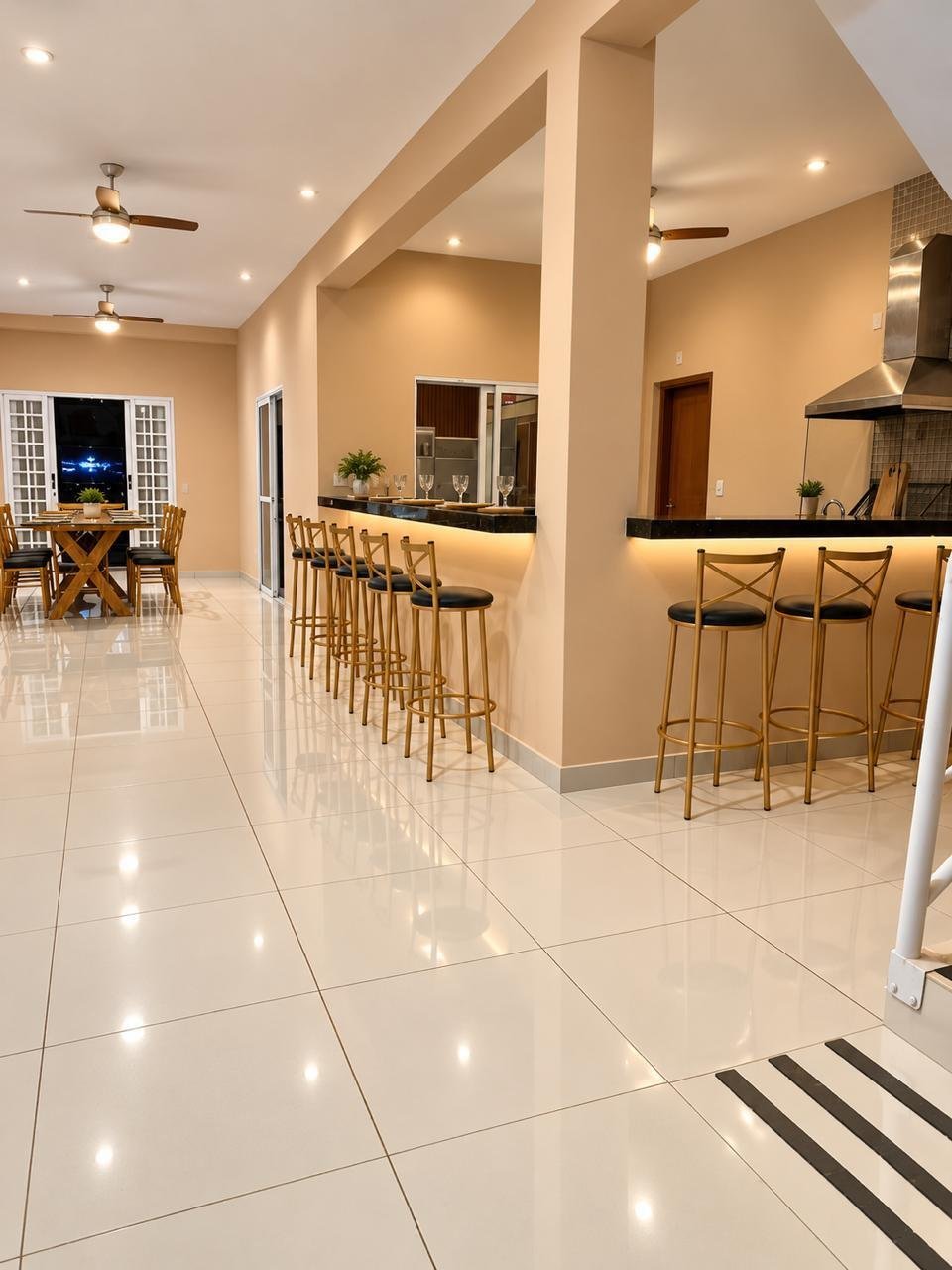 Cozinha e sala de jantar integradas, com bancada, banquetas altas e piso de cerâmica clara